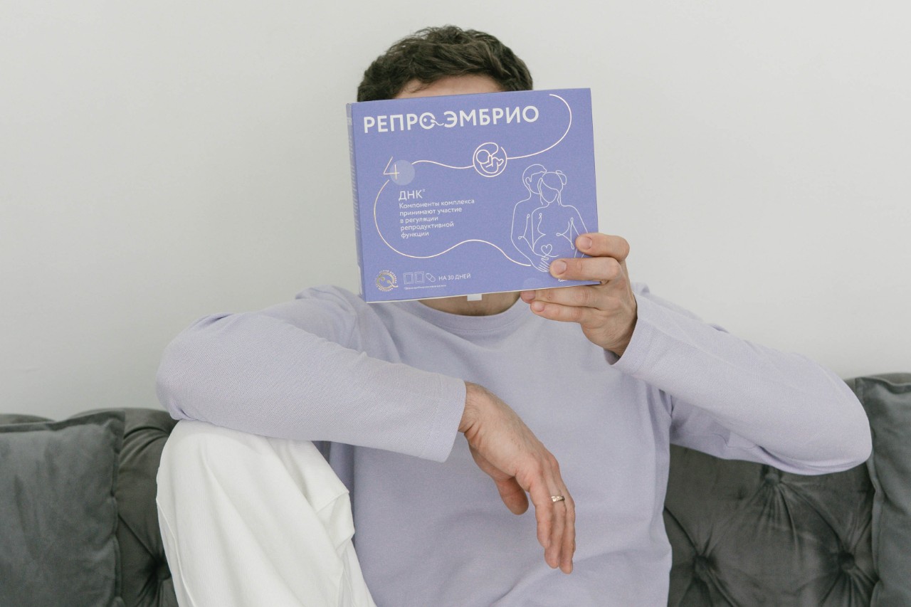 Человек с книгой о репродуктивном здоровье, сидящий на диване, обсуждает поддержку сперматогенеза.