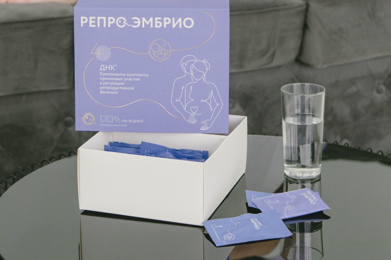 Комплекс репродуктивных витаминов для женщин, упакованный в коробку, рядом с стаканом воды.