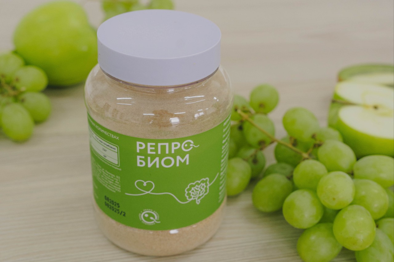 Банка с пробиотиками РЕПРОБИОМ на фоне свежих зеленых яблок и винограда.